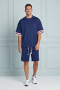 A man wearing a navy blue short-sleeve athletic t-shirt with red and white striped cuffs, paired with matching navy pants with white drawstrings, against a plain white background.