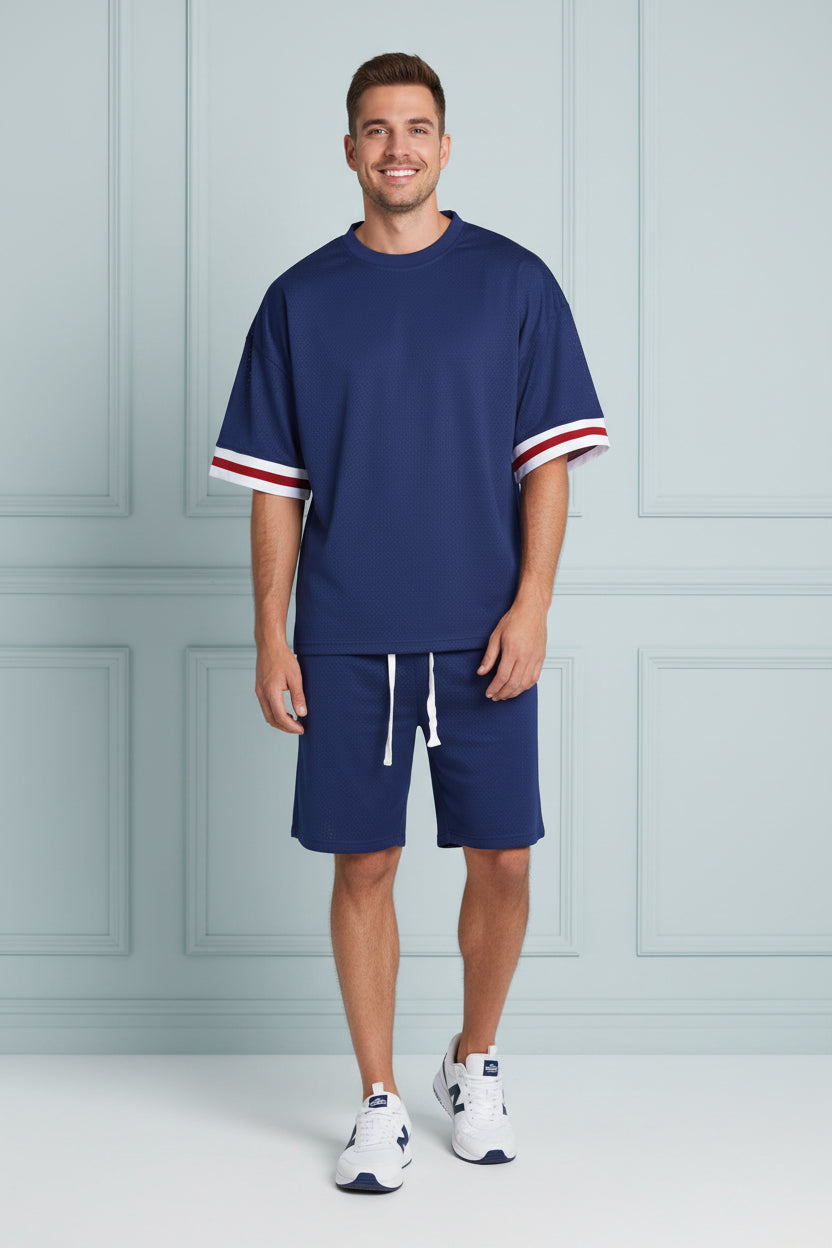 A man wearing a navy blue short-sleeve athletic t-shirt with red and white striped cuffs, paired with matching navy pants with white drawstrings, against a plain white background.